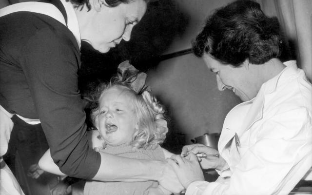 Zwart-wit foto van een kind dat een vaccinatie krijgt toegediend.