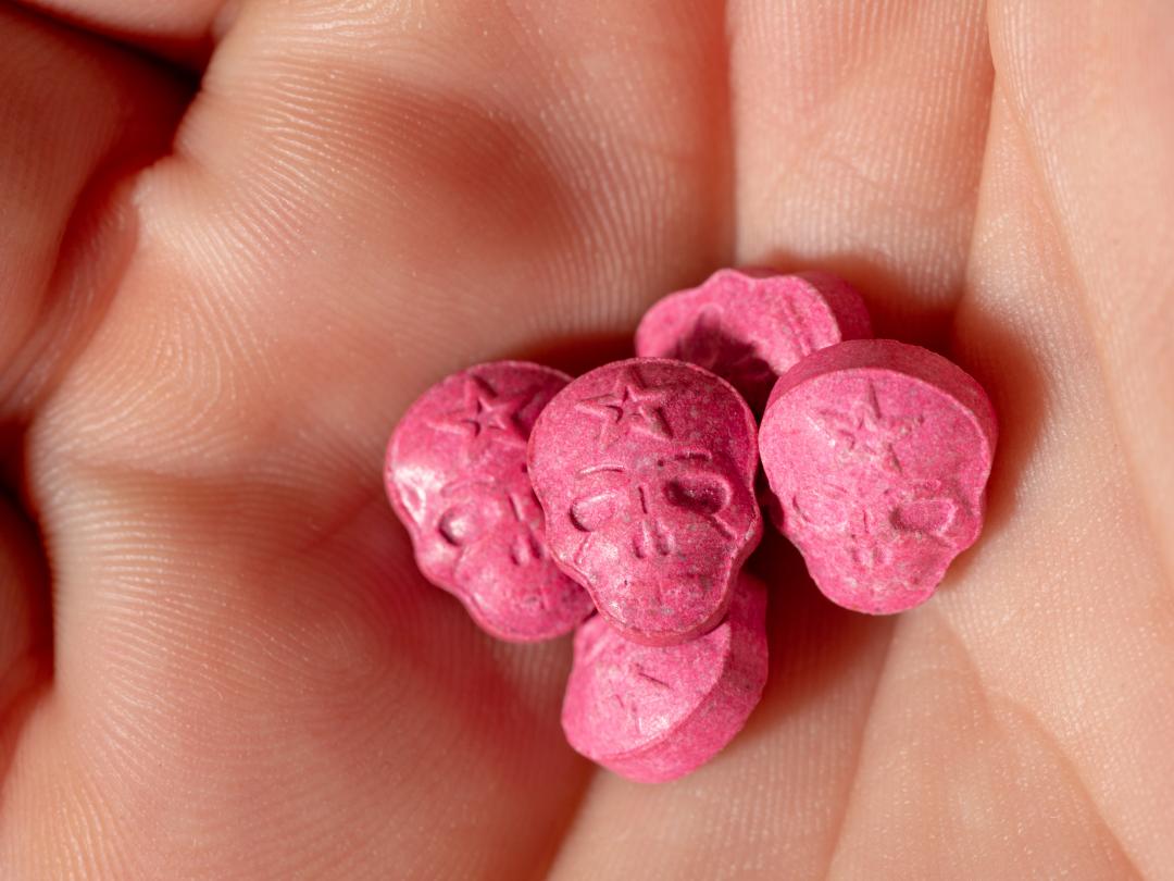 In een handpalm liggen roze pillen in de vorm van doodshoofden.